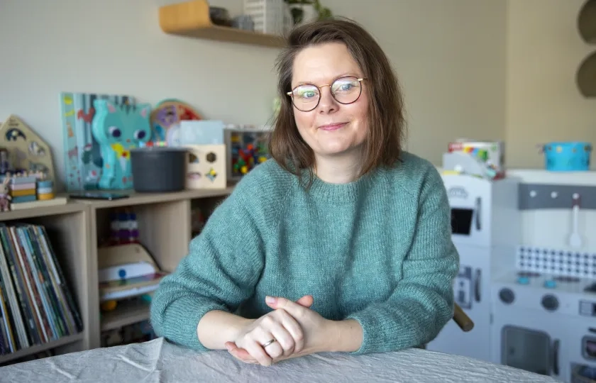 Ann Helen sitter ved et bord og ser p&aring; kameraet